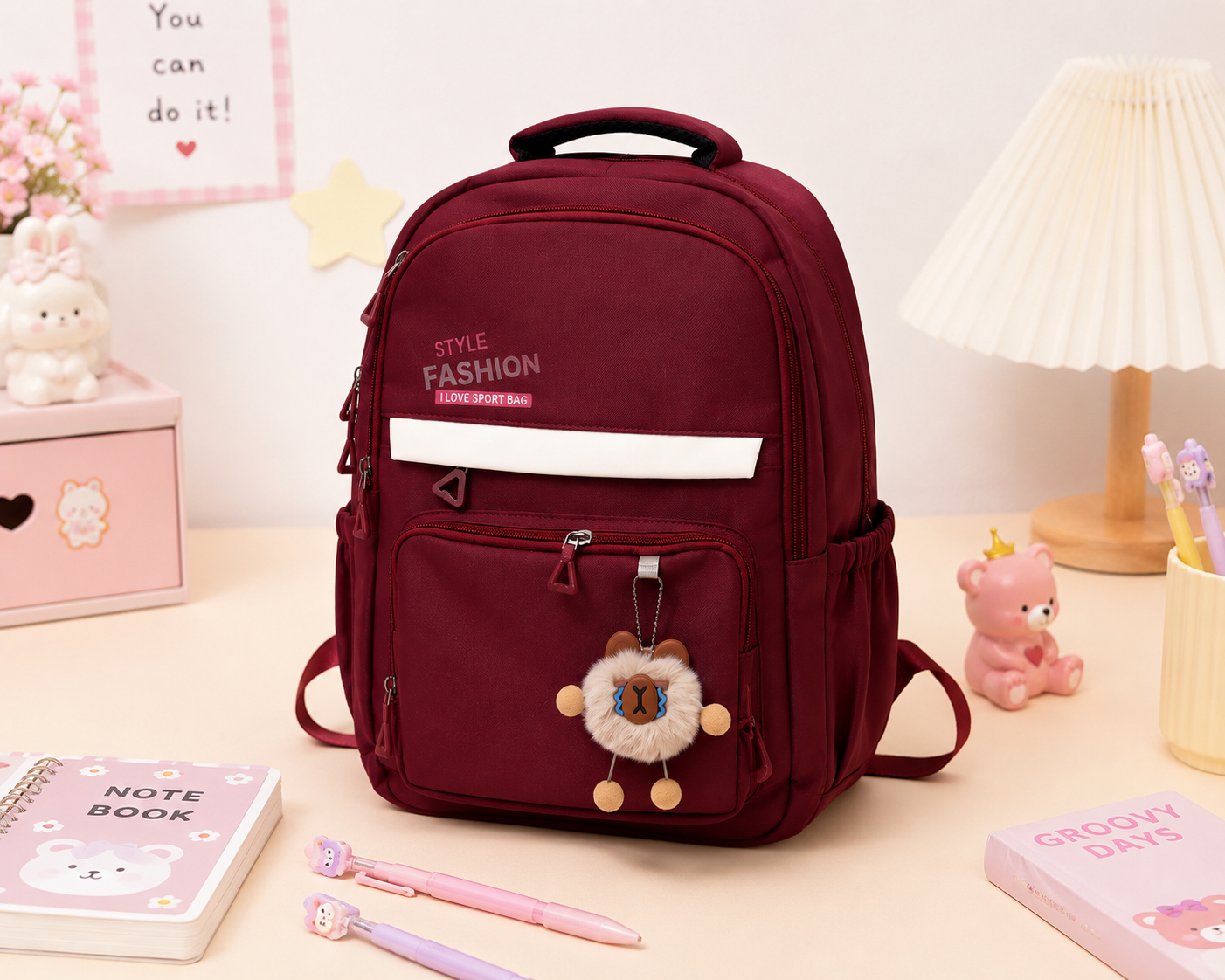 A burgundy nylon backpack with a white horizontal stripe on the front pocket and a cute lion plush keychain, displayed on a light beige desk surrounded by cute school accessories.
