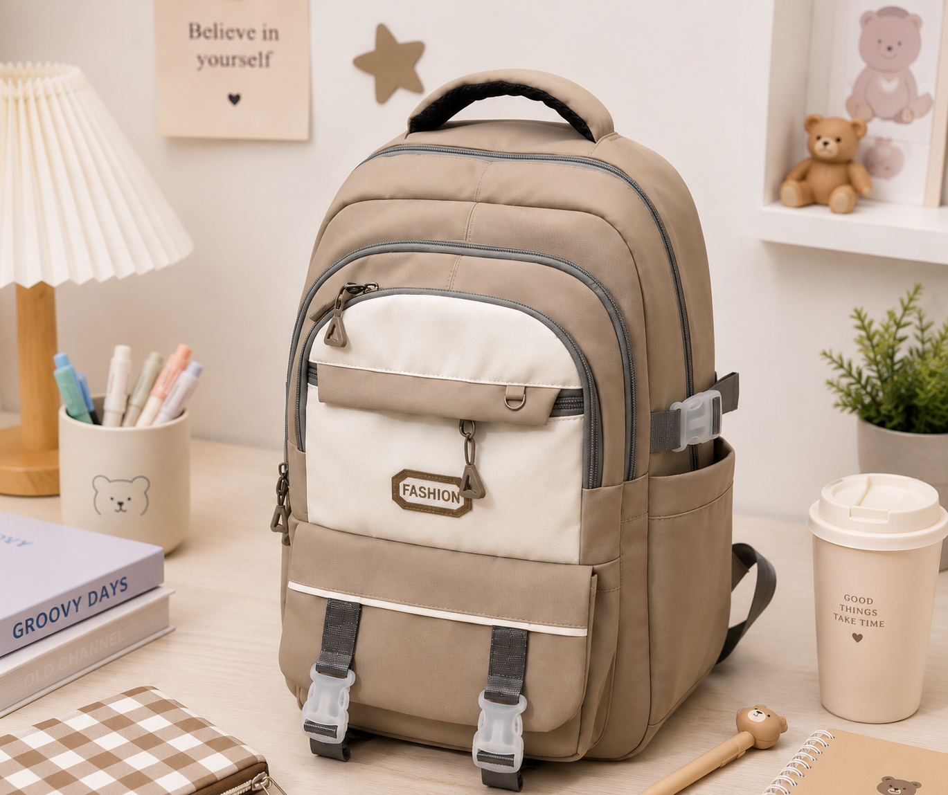 A beige and off-white backpack with gray straps and zippers, styled on a desk with books, a lamp, a plant, and a coffee cup in a cozy room setting.