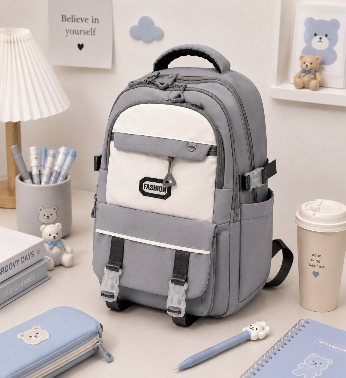 A gray and white backpack with black straps and buckles, styled on a desk surrounded by school and office accessories like a pencil case, notebook, and coffee cup.